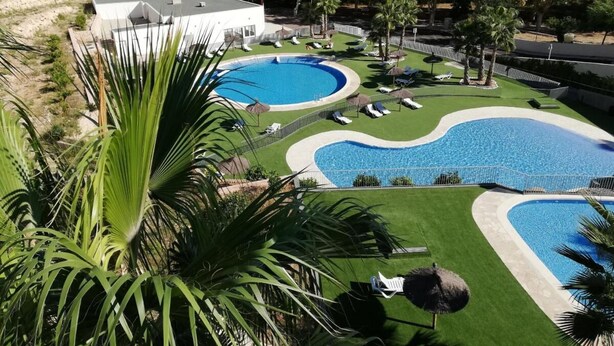 Een resort met meerdere zwembaden, een verzorgd gazon en een groot gebouw op de achtergrond.