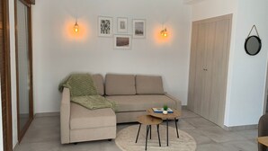 Een moderne woonkamer met een beige bank, een klein rond tafeltje en een groene plaid.