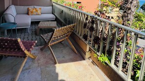 Un balcon avec un canapé, une petite table et un hamac. Il y a une balustrade ornée de plantes et une vue sur une montagne.
