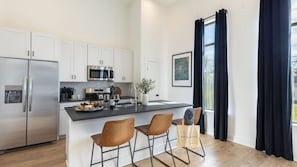 A modern kitchen with white cabinets, stainless steel appliances, a black countertop, and two brown chairs.