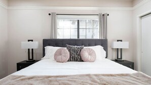 Un lit bien fait, recouvert d’une couverture beige moelleuse, deux tables de chevet avec des lampes et une fenêtre avec des rideaux.