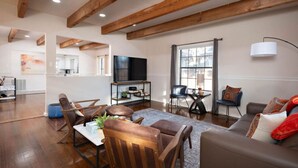 Un salon spacieux avec des poutres apparentes, un grand téléviseur et un coin salon confortable avec un canapé et des fauteuils.