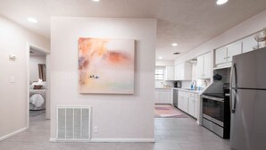 Une cuisine moderne avec des armoires blanches, un réfrigérateur en acier inoxydable et un grand tableau abstrait accroché au mur.