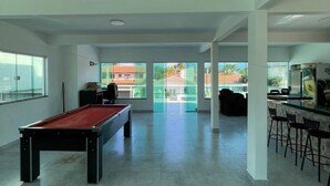 A spacious indoor area with a pool table, a bar area, and large windows offering views of the outside. - Happy FAMILY (Parque Turistico Peruíbe)