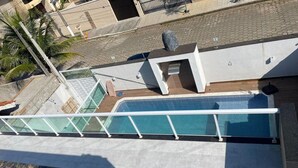 A rooftop pool with a glass barrier, a small seating area, and a palm tree in the background. - Happy FAMILY (Parque Turistico Peruíbe)