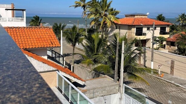 A coastal residential area with a view of the sea, palm trees, and buildings with red-tiled roofs. - Happy FAMILY (Parque Turistico Peruíbe)