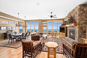 A spacious living room with a stone fireplace, large windows, and a view of the ocean.