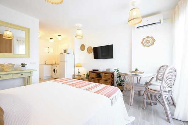 Habitación de hotel con cama, escritorio, silla, televisor, lavadora y mesa de comedor con sillas.