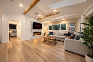 A modern living room with a fireplace, a sofa, a coffee table, and a flat-screen TV mounted above it.
