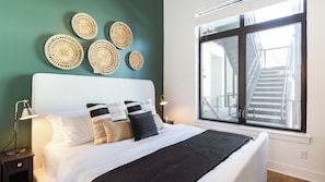 A bed with a white headboard, multiple pillows, a black throw blanket, and a bedside lamp.
