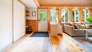 A cozy room with a wooden floor, a sofa with cushions, a small table, and a door leading to a garage. - Lakeside Retreat  with Hot Tub and Bunkie. Sleeps 10 (Otter Lake)
