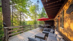 A wooden deck with outdoor furniture, a grill, and a red umbrella. - Lakeside Retreat  with Hot Tub and Bunkie. Sleeps 10 (Otter Lake)