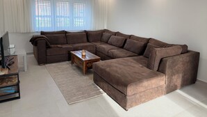 A modern living room with a large L-shaped sectional sofa, a wooden coffee table, and a flat-screen TV on a stand.