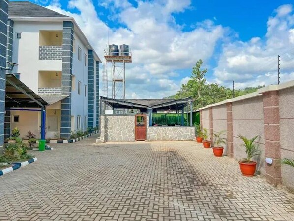 Un patio con un camino empedrado, una zona de estar techada y un tanque elevado de agua.