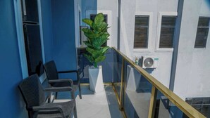 Ein Balkon mit zwei Korbstühlen, einem großen Kübelpflanzen und einem Glasgeländer.