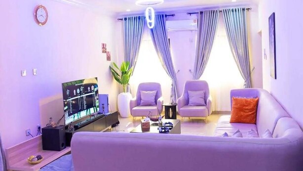Ein modernes Wohnzimmer mit Flachbildfernseher, zwei Sesseln, einem Sofa, einem Couchtisch und einer Topfpflanze.
