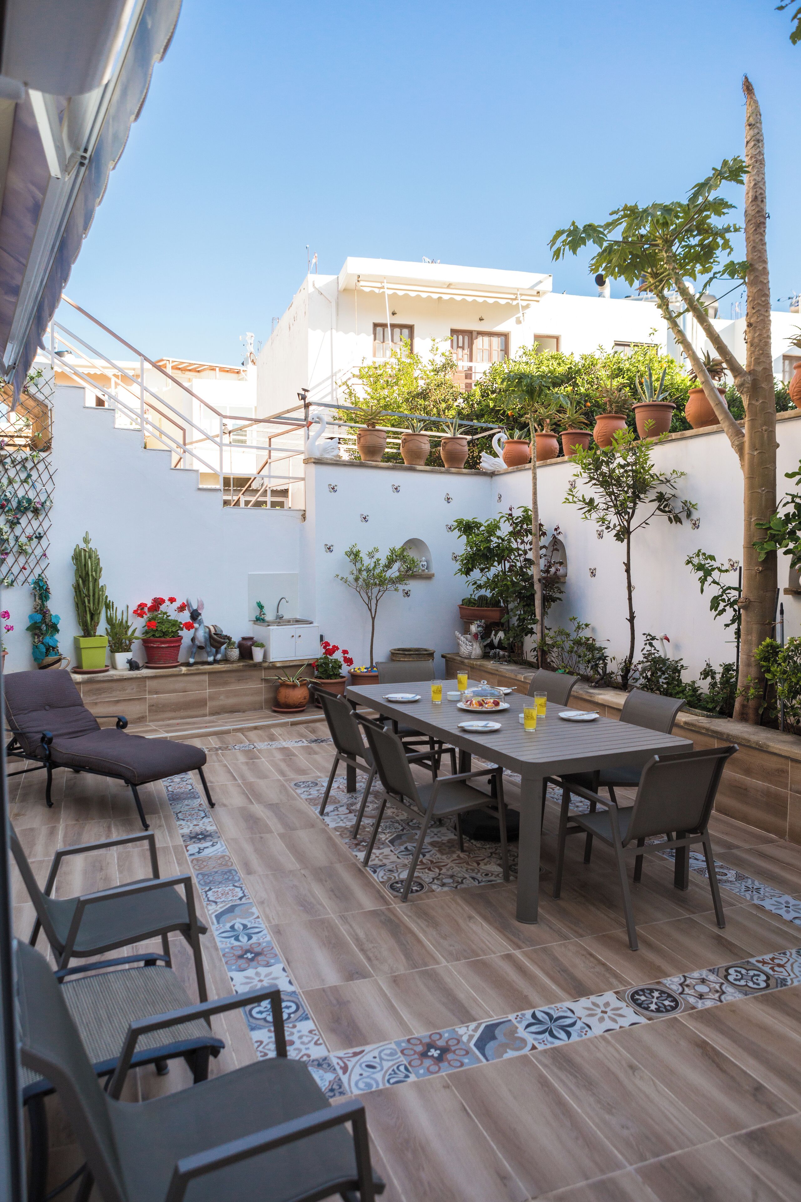 Un patio con una mesa y sillas, rodeado de plantas en macetas y una escalera.