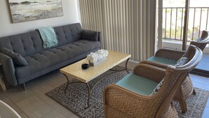 A living room with a grey sofa, a coffee table, wicker chairs, a patterned rug, and a painting on the wall. - Panoramic View and Free Parking (Honolulu)