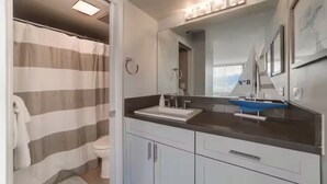 A bathroom with a striped shower curtain, a white sink, a mirror, and a towel rack. - Panoramic View and Free Parking (Honolulu)