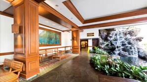 A lobby with wooden paneling, a large painting, seating area, and a waterfall feature. - Panoramic View and Free Parking (Honolulu)