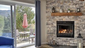 A modern living room with a stone fireplace, a blue sofa, and a view of the outdoors through large sliding glass doors.