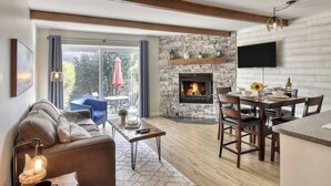 A modern living room with a stone fireplace, wooden beams, a dining area, and a TV mounted on the wall.