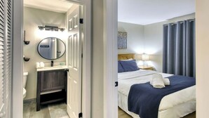 A hotel room with a bed, a bedside table with a lamp, a bathroom with a toilet, a sink, and a mirror.