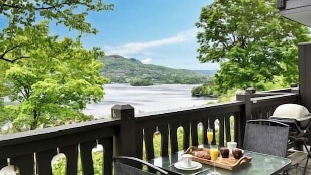 An outdoor dining area with a table set for two, overlooking a river and hills.