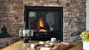 A wooden table with a charcuterie board, wine glasses, and a fireplace with a stone wall.