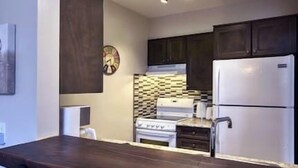 A kitchen with dark wooden cabinets, a white refrigerator, a stove, and a clock on the wall.