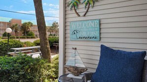 A welcome sign with palm trees and a beach umbrella, a wicker chair, and a small table with a decorative item. - Cozy 1-bedroom condo in wonderful Destin with AC (Destin)