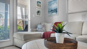 A modern living room with a beige sofa, a round coffee table with a woven basket, and a potted plant. - Cozy 1-bedroom condo in wonderful Destin with AC (Destin)