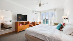 Une chambre d’hôtel avec un grand lit, une télévision, un bureau avec une chaise, un miroir et un balcon avec vue.