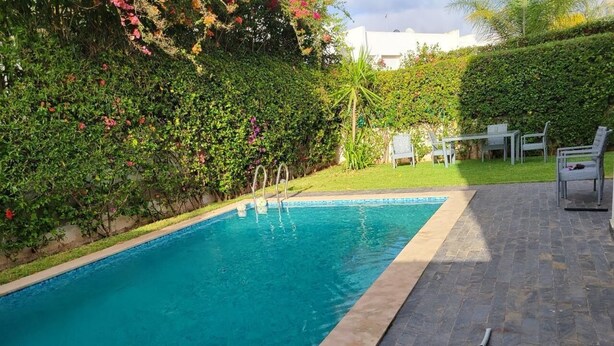 Une piscine rectangulaire dont les bords sont recouverts de carreaux, entourée d’une terrasse en pierre.