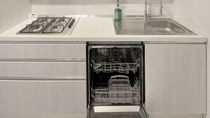 A modern kitchen with white cabinetry, a stainless steel range hood, a built-in dishwasher, and a sink with a faucet. - Thomas House on Train Tracks (Venezia)