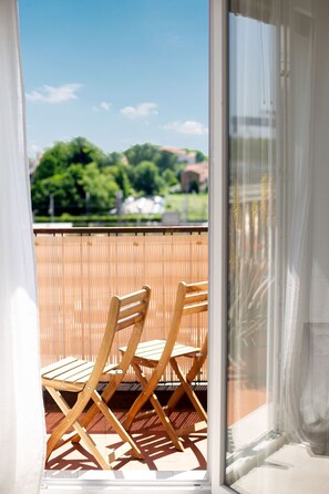 Een balkon met twee houten stoelen en uitzicht op groen en gebouwen in de verte.