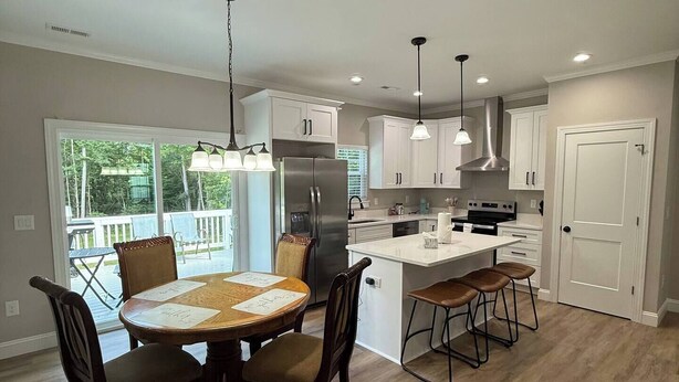 A modern kitchen with white cabinets, a stainless steel refrigerator, and a dining area with a wooden table and chairs.