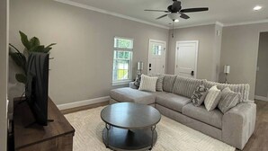 A spacious living room with a large sectional sofa, a round coffee table, and a ceiling fan.