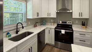 A modern kitchen with white cabinets, a stainless steel stove, and a window with blinds.