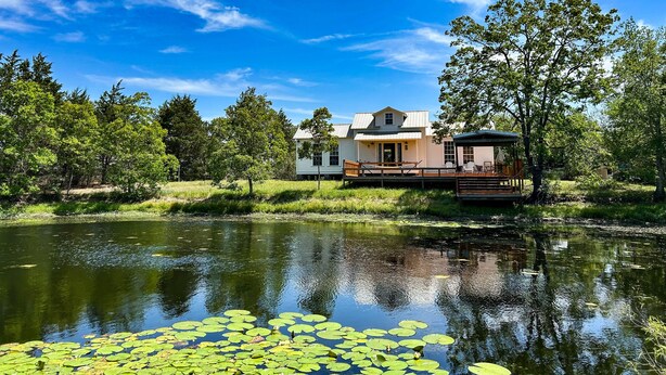 A lakeside cabin with a deck, surrounded by trees and a clear sky. - The Bee Farm, House + Studio 15 Mins to Round Top (Ledbetter)