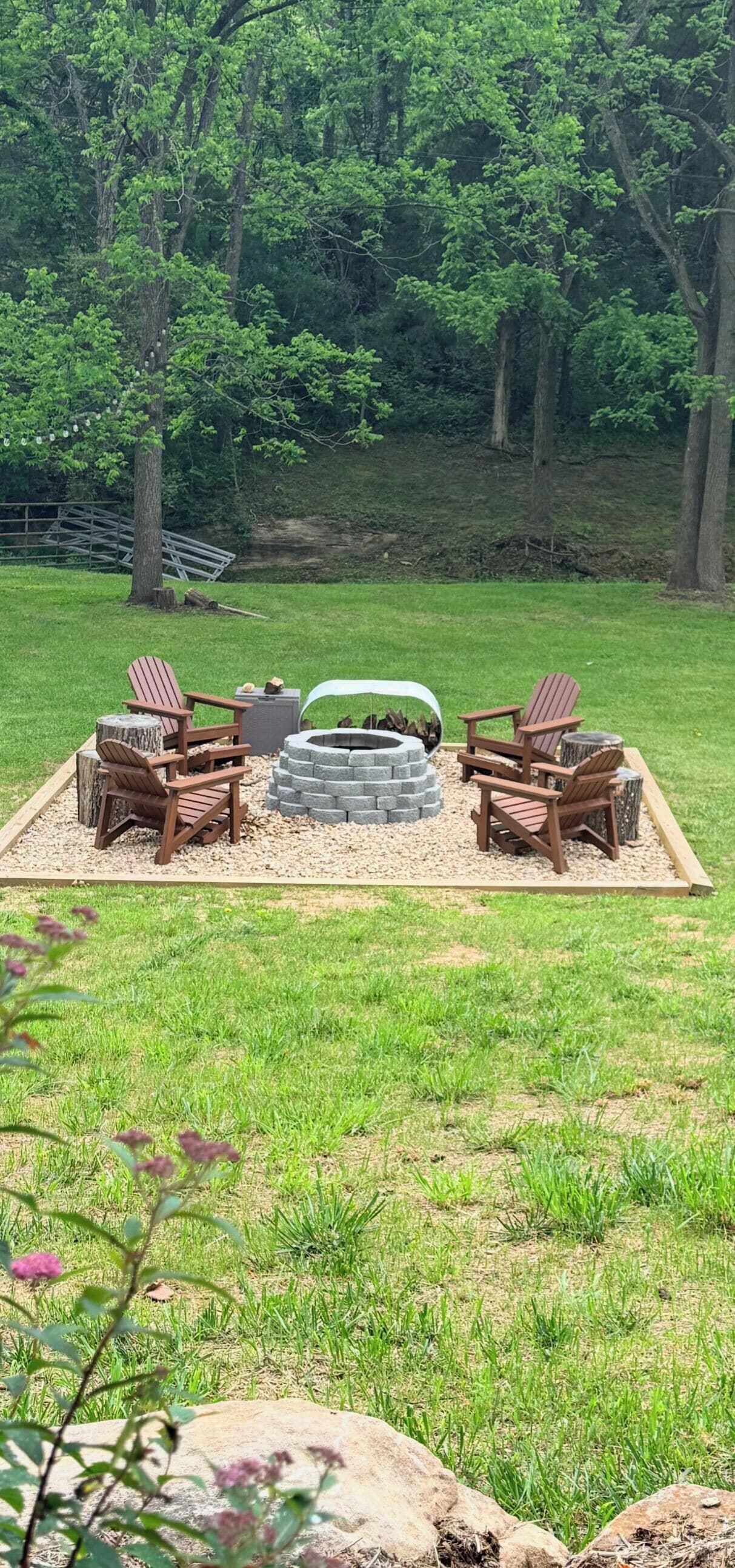 A fire pit with seating and a wooden deck in a grassy area.
