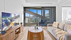 A modern living room with a large flat-screen TV, a round coffee table, a sofa, and a chair. - Jewel - 2 Bed Chic Unit - Q Stay (Surfers Paradise)