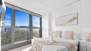A modern bedroom with a large window, a bed with a white headboard, a bedside table with a lamp, and a city view. - Jewel - 2 Bed Chic Unit - Q Stay (Surfers Paradise)
