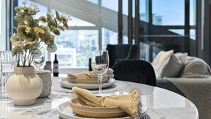 A dining table set with plates, glasses, and a vase of flowers. - Jewel - 2 Bed Chic Unit - Q Stay (Surfers Paradise)