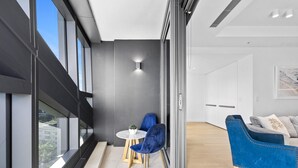 A modern interior with a blue velvet sofa, a round table with a small plant, and a glass partition. - Jewel - 2 Bed Chic Unit - Q Stay (Surfers Paradise)