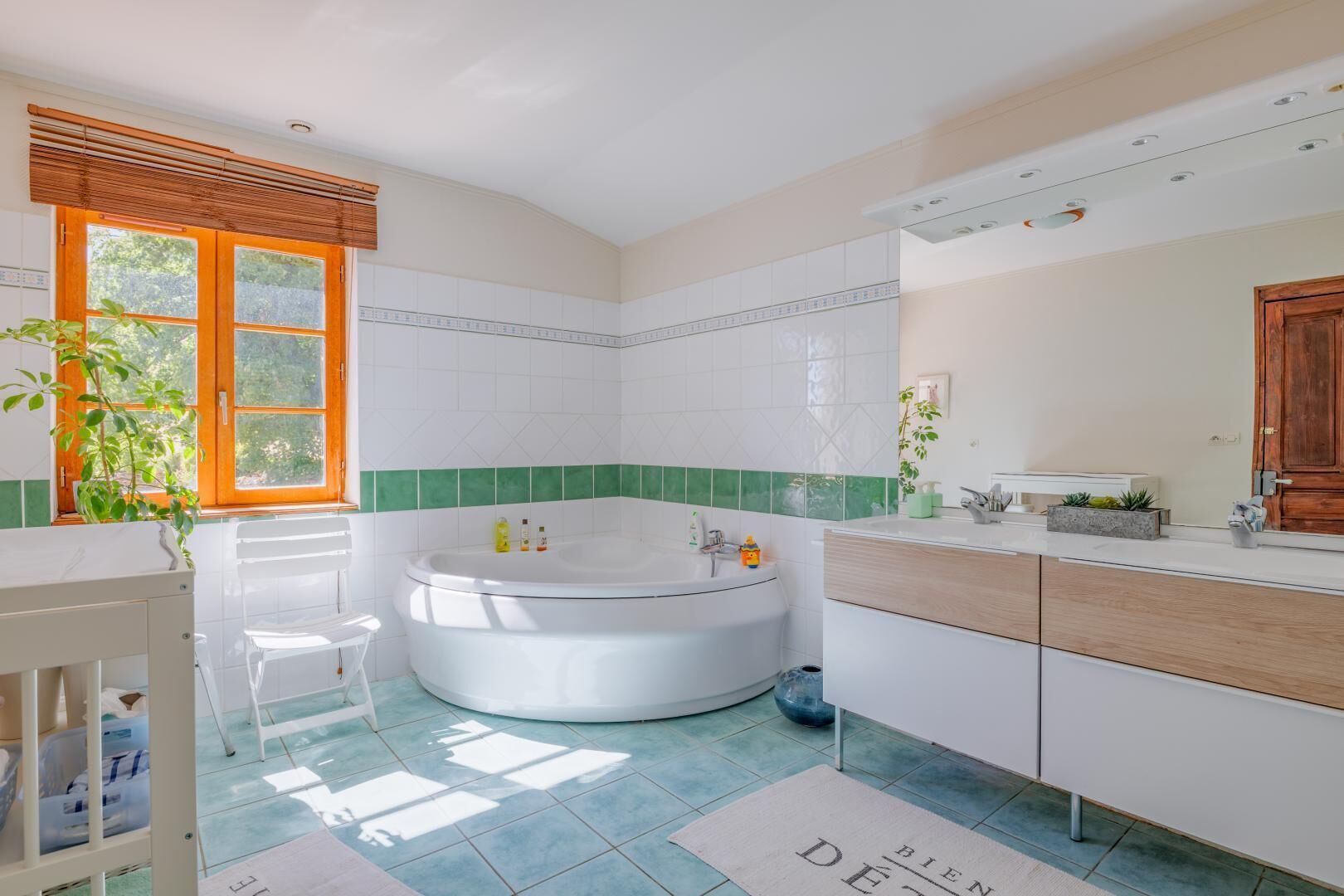 Ein modernes Badezimmer mit freistehender Badewanne, einem Waschtisch mit Spiegel und einem Fenster mit Jalousien.