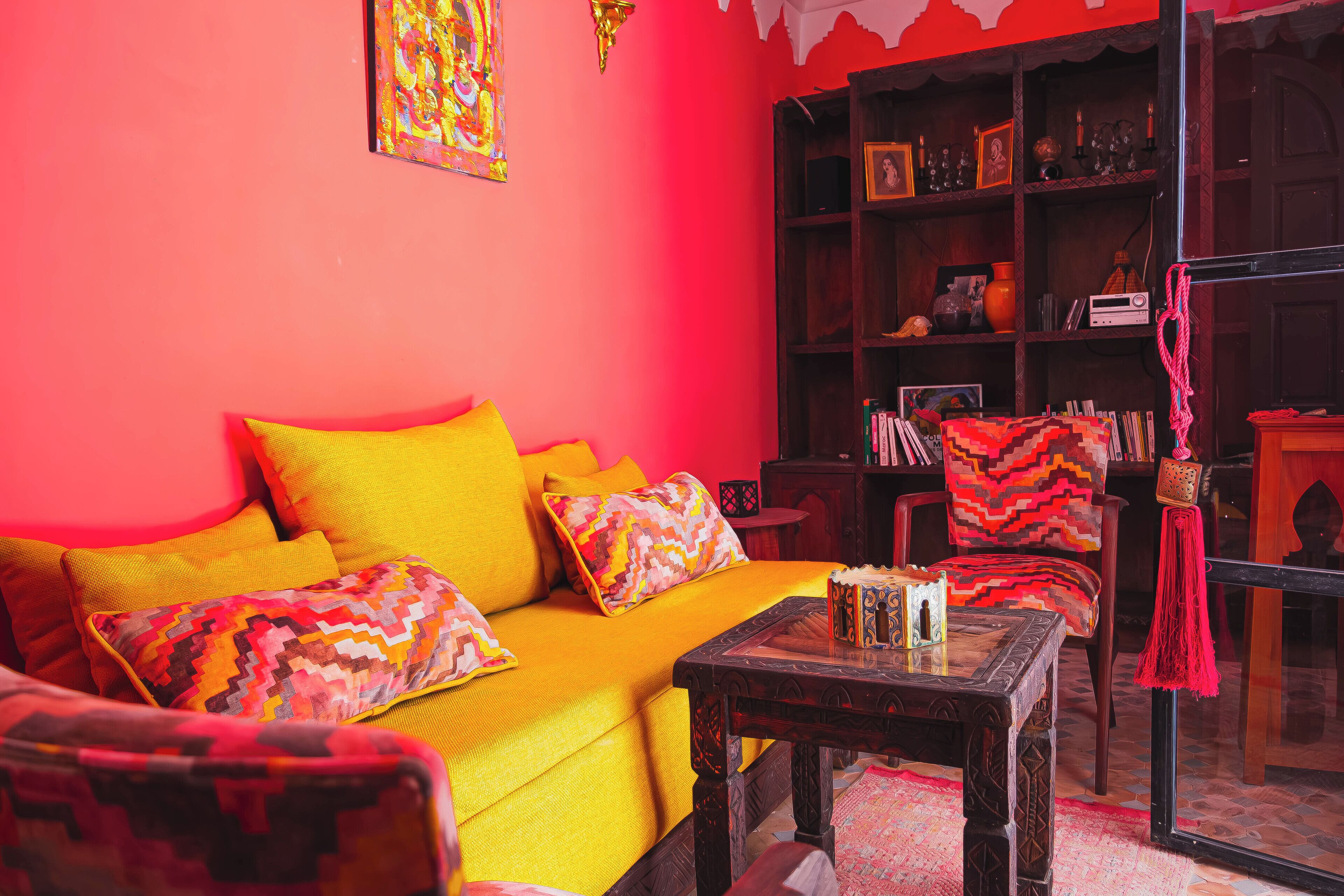 Una habitación con un sofá amarillo brillante, una mesa de centro de madera y una estantería llena de objetos varios.