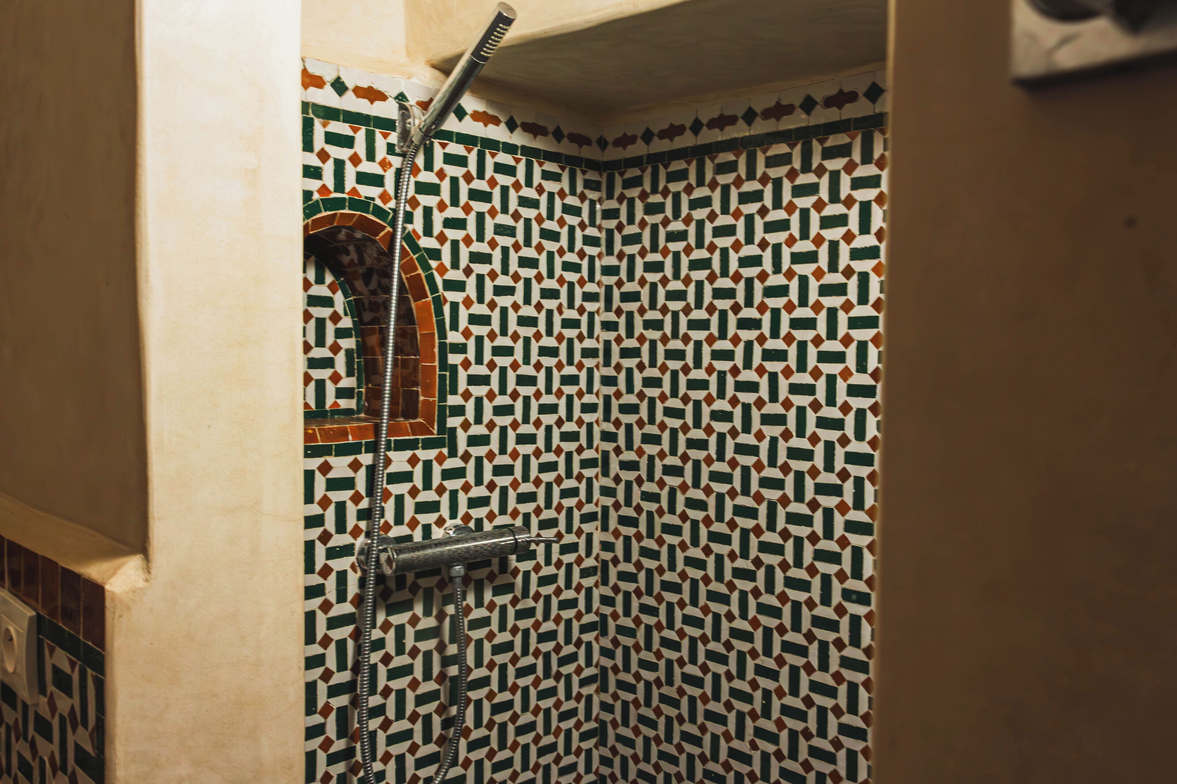 A shower with a geometric tile pattern and a handheld showerhead.