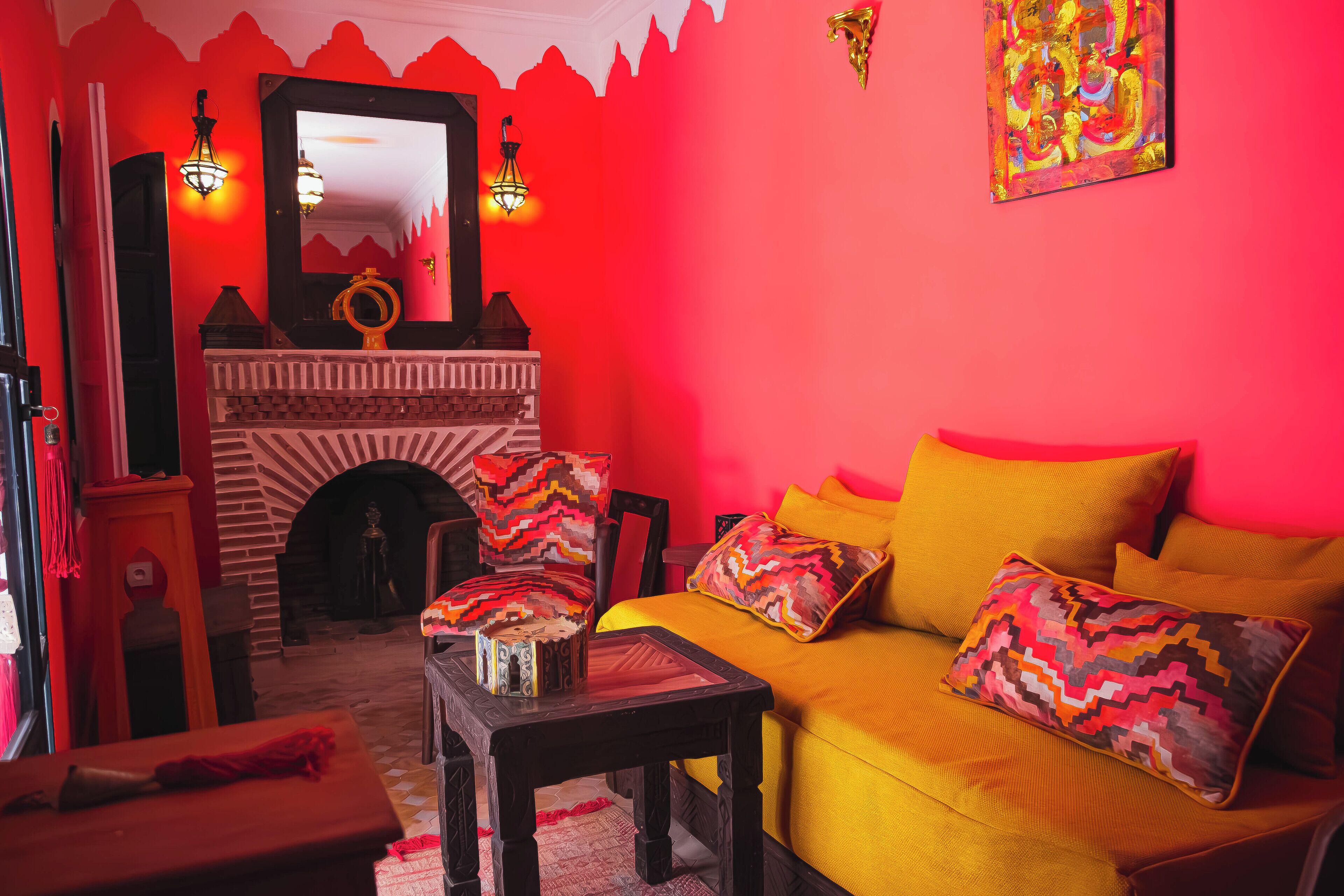 Une pièce chaleureuse avec un mur rouge, une cheminée, un canapé agrémenté de coussins colorés et une table en bois.