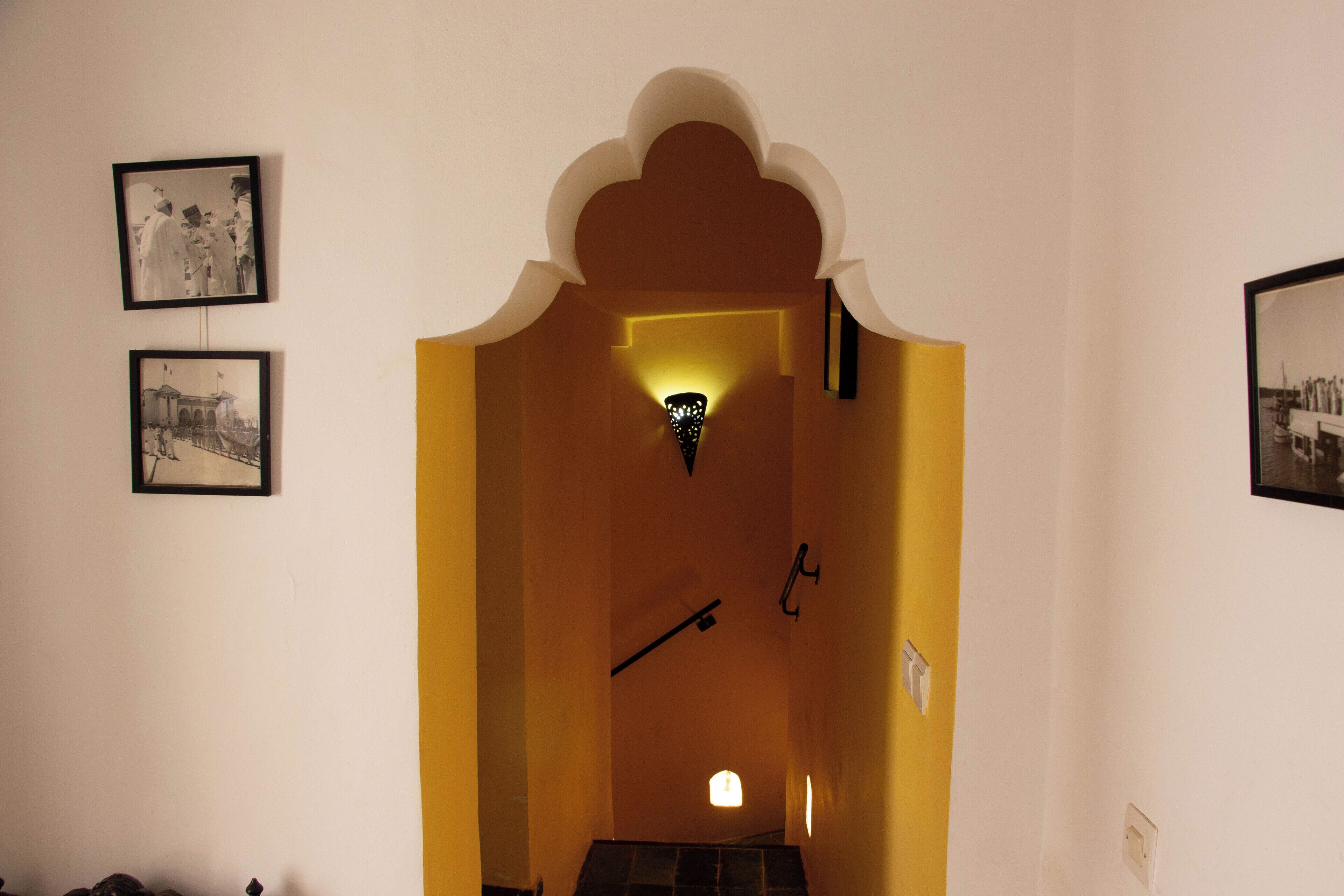 Un pasillo con un arco decorativo, fotografías enmarcadas en las paredes y una lámpara en el centro.